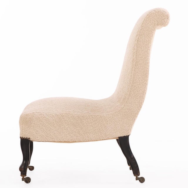 featuring a graceful arched back and low seat raised on turned ebonized legs terminating in brass casters. The chair has...