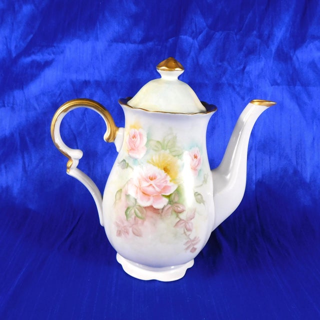 This is a hand painted and signed white teapot with a pink floral design with greenery. The teapot is trimmed in gold and...