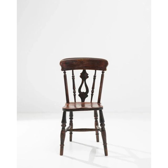 A decorative back splat and expressive patina give this wooden chair a poetic character. Made in the UK circa 1900, the...