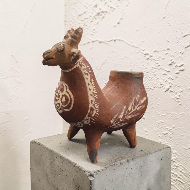 A charming hand-painted Peruvian folk art pottery vessel formed as a stylized llama or alpaca figure. Crafted in warm...