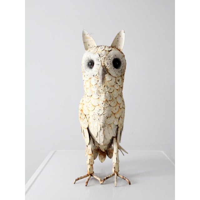 A vintage handmade metal owl sculpture featuring layered cut-metal featherwork, oversized dark eyes, and an aged painted...