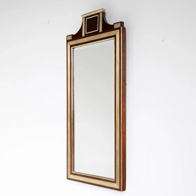 Large wall mirror with brass profiles and mahogany veneered frame as well as a gable end rising in the middle. The mirror...