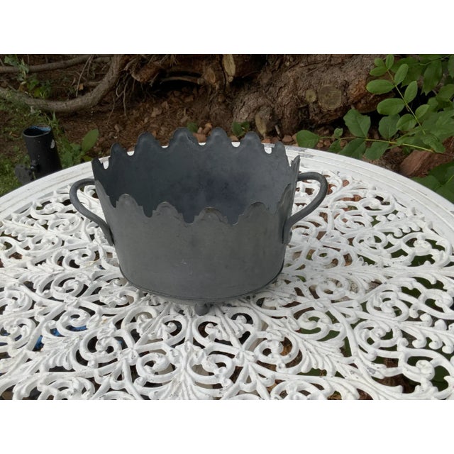 Pewter colored metal cachepot with scalloped top rim on bun feet. Fluted metal handles.