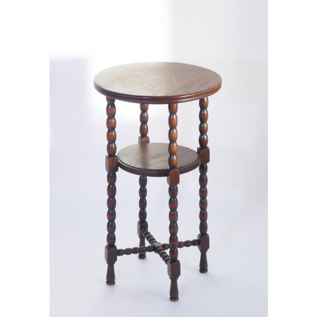 A small wooden side table with bobbin style legs in round shape with two tiers. The wood has a beautiful grain pattern....
