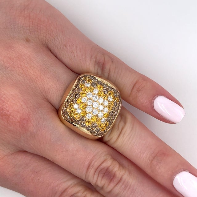 This ring features a cluster of round brilliant cut white and brown diamonds, complemented by yellow sapphires. The dome-...