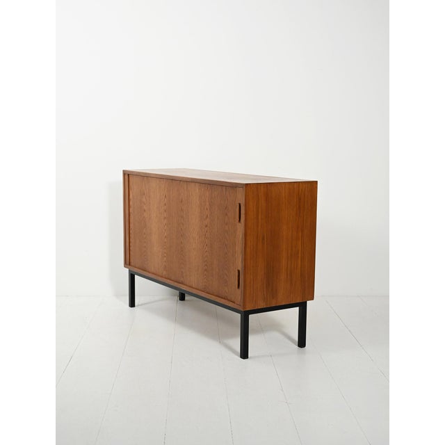 Scandinavian teak sideboard from the 1960s with a side roller door, a compartment with a double shelf, and black metal...