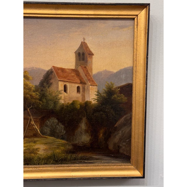 This 19th century oil on canvas depicts a serene French church nestled within a pastoral landscape, rendered in soft,...