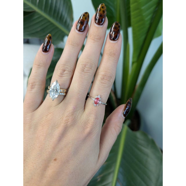 A 0.63-carat padparadscha sapphire oval sits at the centre of this solid 14K white gold ring, framed by eight earth-mined...