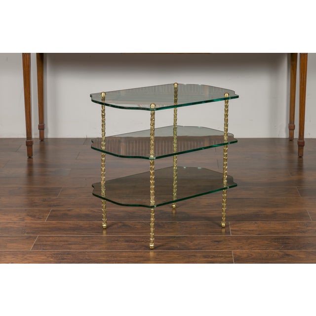 A vintage brass tiered table from the mid-20th century, with glass shelves and foliage motifs. Created during the...