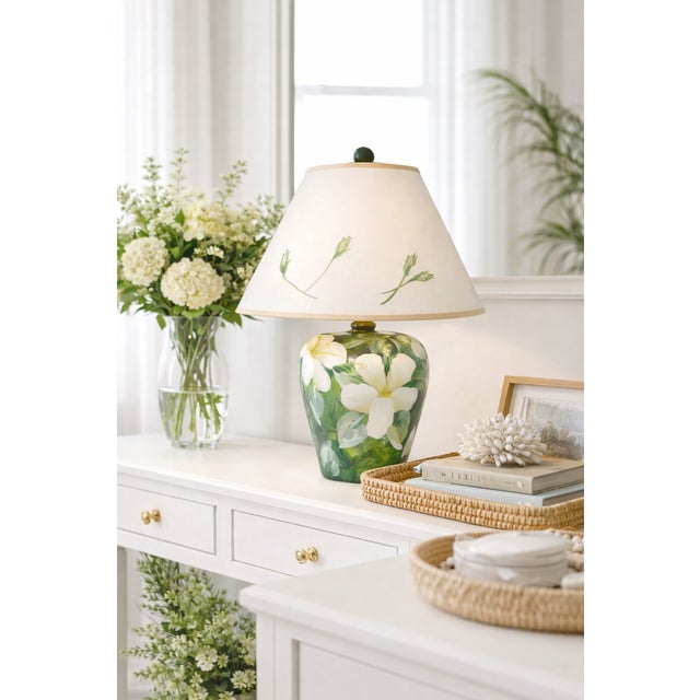 A refined vintage hand-painted table lamp featuring magnolia blossoms set among lush green foliage, paired with a...