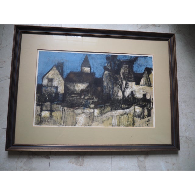 A framed, signed lithography 'Village dans la Nuit' by French artist Bernard Cathelin. Dark wood frame with a blue accent...
