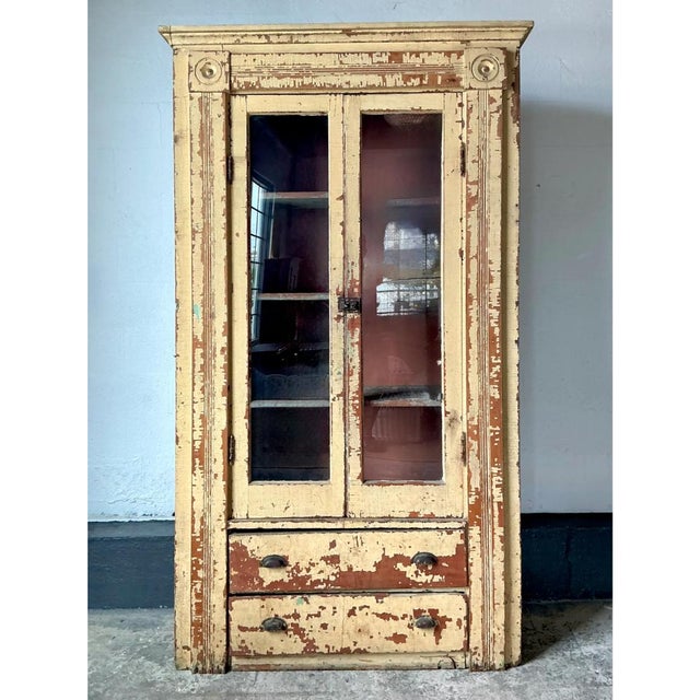 This vintage cabinet rises in a tall, architectural silhouette, crowned with a projecting cornice molding and flanked by...