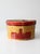 A vintage 1930s Dunlap New York hat box featuring bold red and black graphics against a warm gold patterned ground,...
