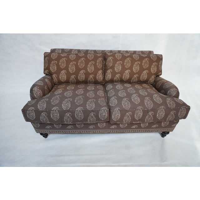 Cambridge Loveseat in a light brown linen paisley upholstery. The sofa has beautiful, turned dark wood legs in the front....
