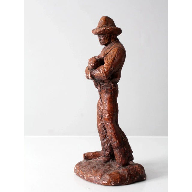 This is a vintage cowboy statue. The plaster faux bois statue envisions a cowboy holding a piglet and reads "Maverick" at...