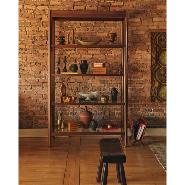 A striking vintage brass étagère featuring a clean architectural frame and four glass shelves. This piece balances...