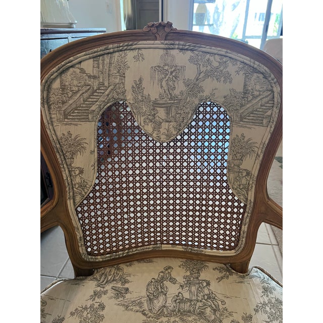 Elegant vintage French-style bergère armchair featuring a classic carved wood frame, curved arms, and a cane back inset....