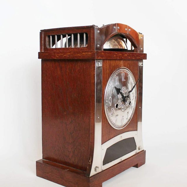 An Arts & Crafts oak wood and silver plated on copper clock. Red Glass panel underneath numbered clock face. Dimensions: H...