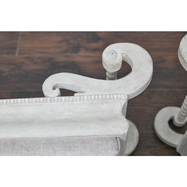 A pair of Rococo style Continental 1920s white painted ottomans with S-Scroll legs. Elevate your home with this stunning...