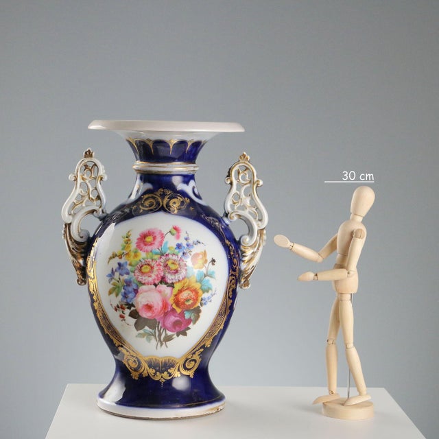 A pair of cobalt blue porcelain vases with hand-painted floral decorations enclosed in gold reserves. Elaborate handles on...