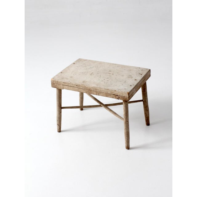 Antique primitive stool with a worn, timeworn painted surface and a quiet, understated presence. The faded tones and...