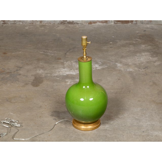 A luminous apple green porcelain vase, now configured as a single-socket table lamp, mounted on a circular giltwood base....