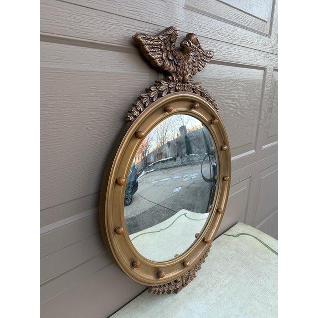 A gorgeous Federal or Regency style convex bullseye wall mirror featuring a carved eagle with open wings standing on olive...