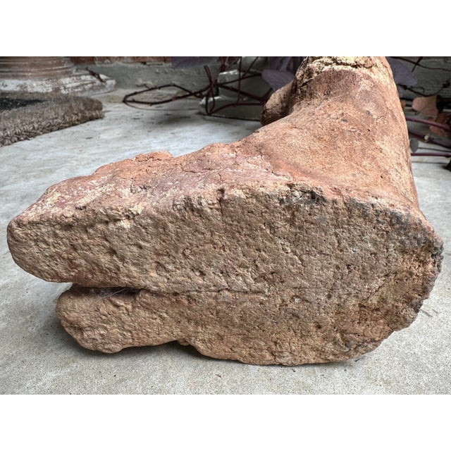 An arresting, hand-formed terracotta sculpture of a seated female figure, rendered in a primitive, raw style that evokes...