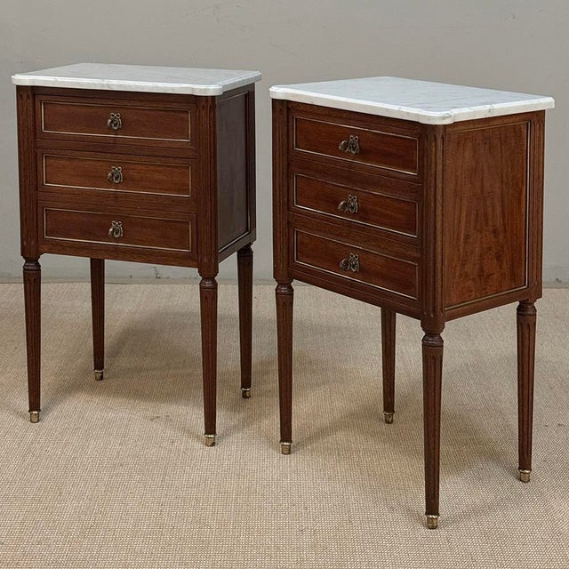 A distinguished pair of French Louis XVI style nightstands from the early twentieth century, reflecting the refined,...