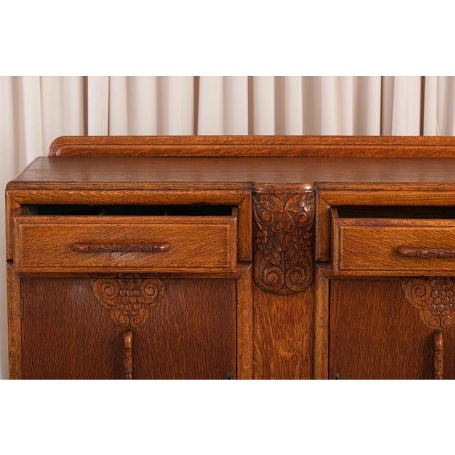 An oak sideboard with the stepped, rounded outlines of the Art Deco period. Two drawers with carved handles sit above two...