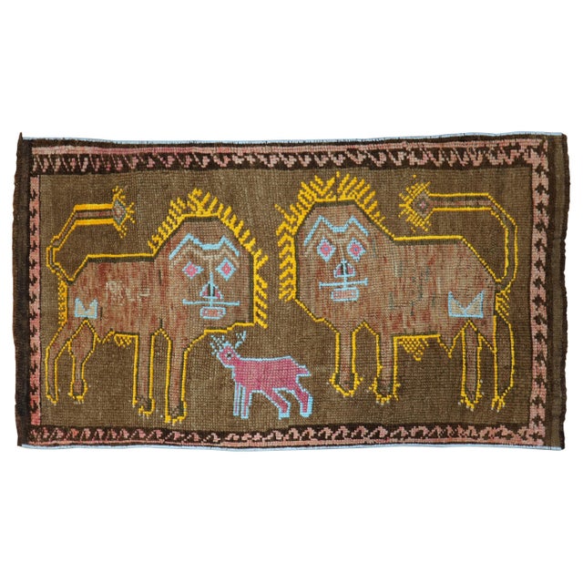 A late 20th century Turkish rug depicting 2 lions outlined in yellow and a pink sheep outlined in light blue on a brown...