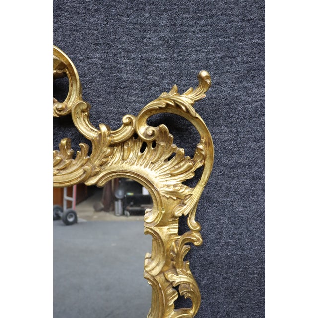 Mid-century Italian Rococo Revival wall mirror featuring an elaborately hand-carved giltwood frame with deeply pierced...