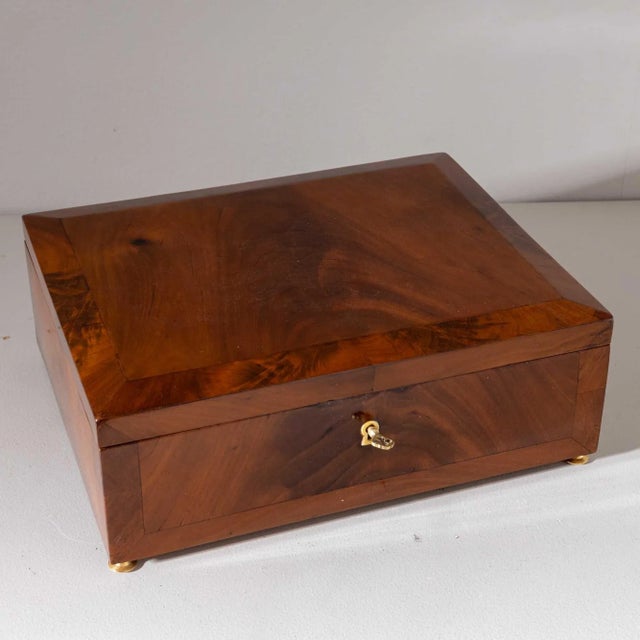 Small rectangular casket with slightly beveled lid and filling-shaped veneer pattern made of walnut. The casket stands on...