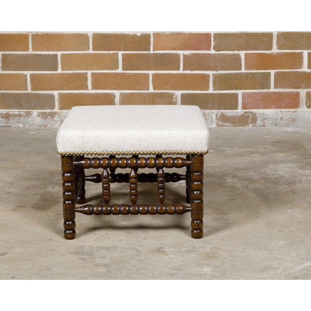 An English bobbin leg stool from the 19th century with new linen upholstery secured with a brass nailhead trim. This...