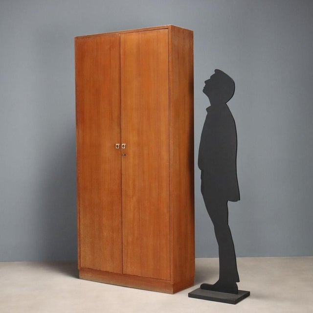 2-door wardrobe with adjustable shelves, in teak veneer. This piece is attributed to the mentioned designer/maker. It has...