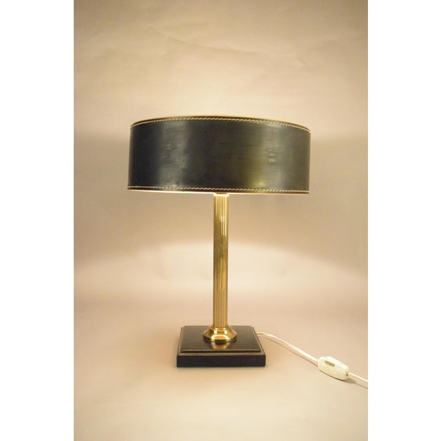 A sophisticated Jacques Adnet table lamp, combining a fluted brass column with a square base and shade wrapped in black...