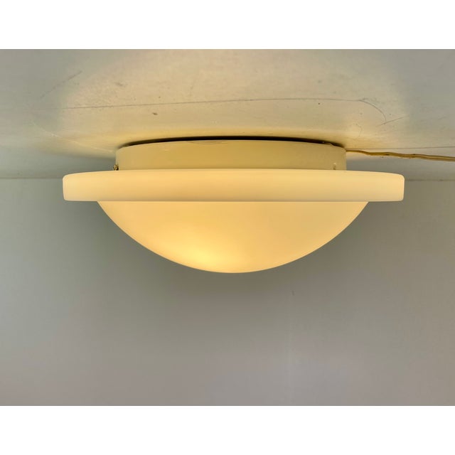 Beautiful minimalist flush-mounted ceiling lamp with a white opaline glass diffuser in saucer shape mounted on a white...