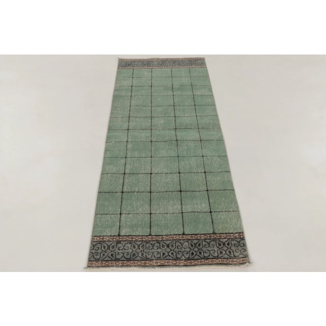 Hand-knotted in wool, this vintage Turkish 2x7 runner rug from circa 1950–1960 features a mint green geometric field with...