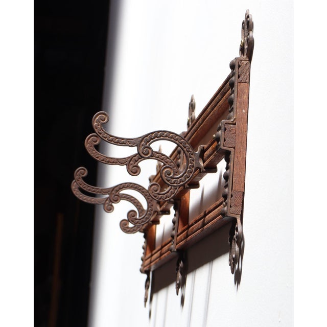 Antique oak and cast iron hanging coat/hat rack with four sliding hooks and three ornately decorated brackets with...