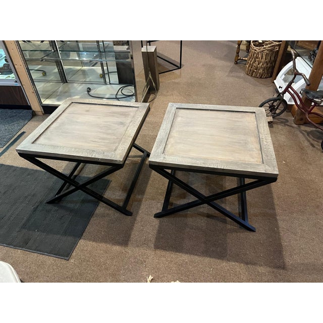 A stylish pair of vintage wood and iron side tables featuring warm natural wood tops set on sleek black metal folding-...