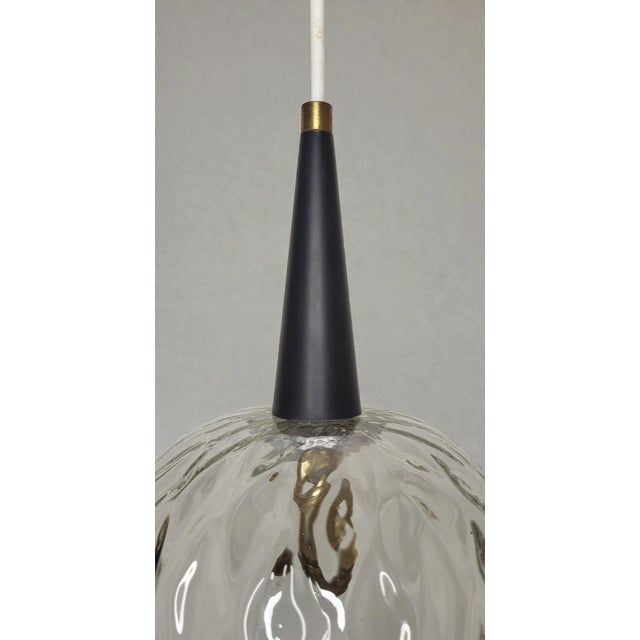 Glass pendant light, 1960s. Clear glass diffuser with undulating relief and a serrated lower edge. Conical black lacquered...