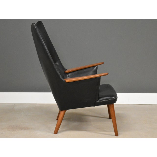 An original teak Mama Bear chair designed by Hans J. Wegner for AP Stolen in black leather. Made in Denmark. Circa 1960’s....