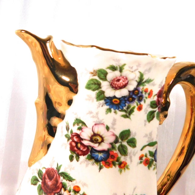 This is an unmarked pink and white teapot or chocolate pot with a multicolor floral design and a gold painted handle and...