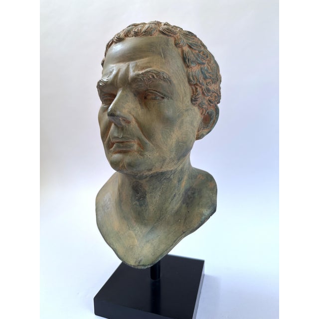 A powerful patinated bronze portrait bust inspired by Classical Greco-Roman sculpture, mounted on a modern black museum-...