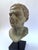 A powerful patinated bronze portrait bust inspired by Classical Greco-Roman sculpture, mounted on a modern black museum-...
