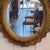 An oval wall mirror set within an ornate gilt gesso frame in a period style, featuring a deeply molded surround with...