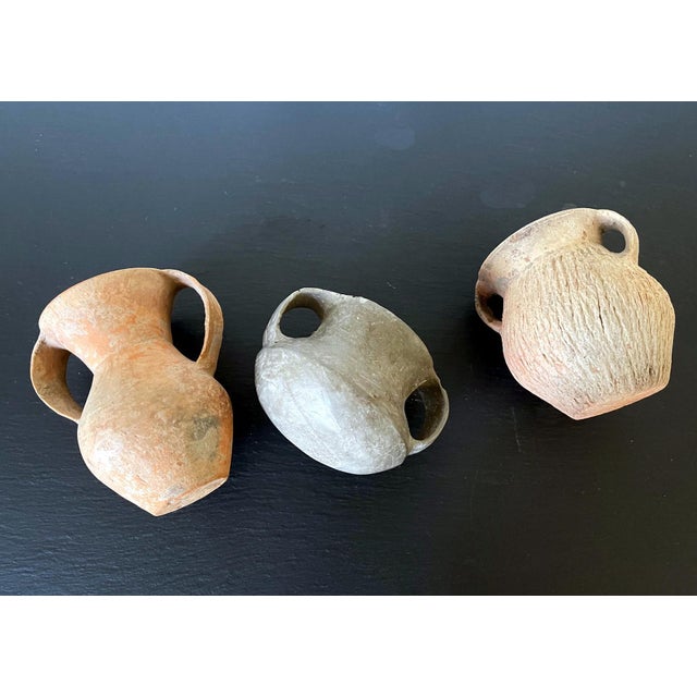 A collection of three small Chinese Neolithic pottery jars consisting a red slender jar with large double ears, a grey and...