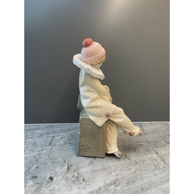 An elegant and expressive Lladro porcelain figurine depicting a contemplative jester on a textured pedestal. This...