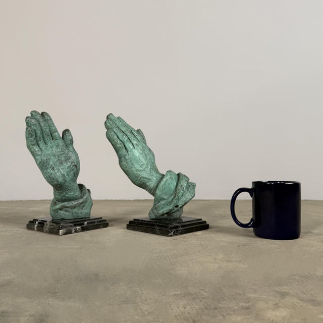 Striking pair of hand cast bronze sculptures depicting clasped hands in a gesture of prayer, mounted on solid black marble...