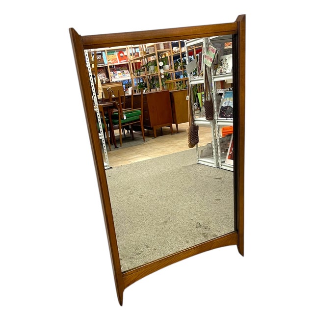 This mid-century modern wall mirror features a sculpted wood frame with clean lines and gently curved lower and upper...
